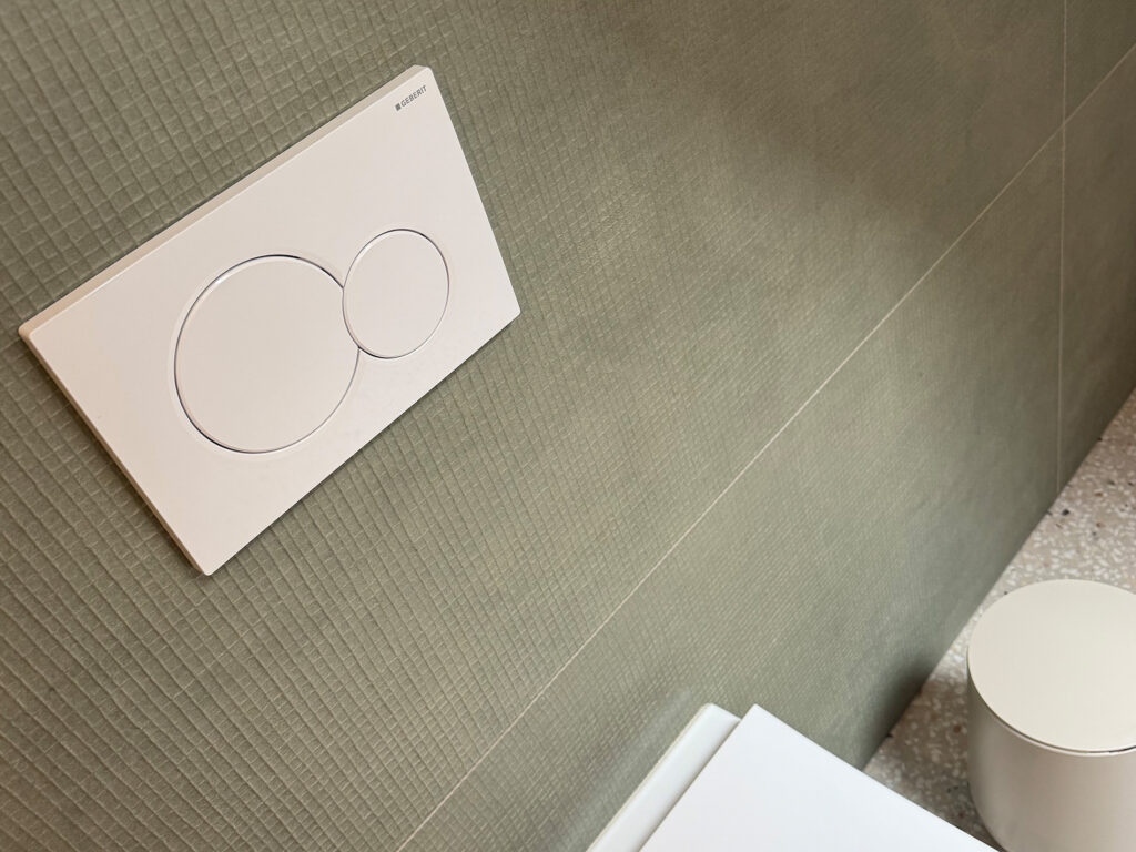 Witte Geberit bedieningsplaat met ronde drukknoppen boven Catalano hangtoilet in Brusselse badkamerrenovatie