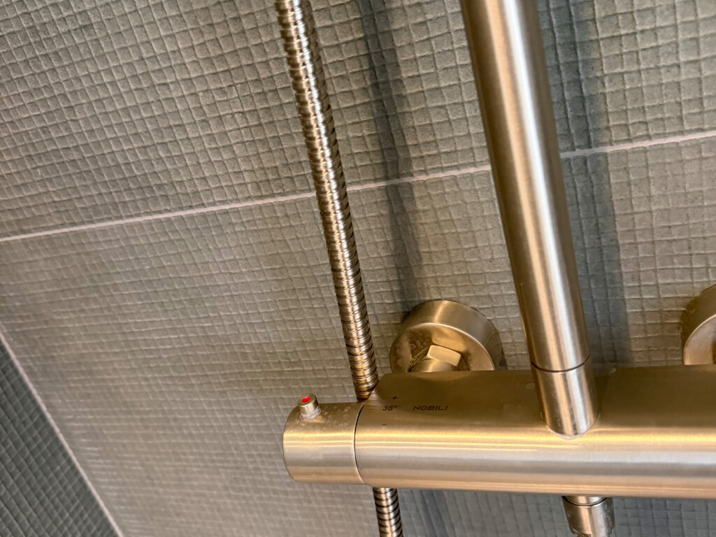 Detail van Nobili thermostatische douchekraan in geborsteld nikkel tegen olijfgroene tegels in badkamerrenovatie Brussel