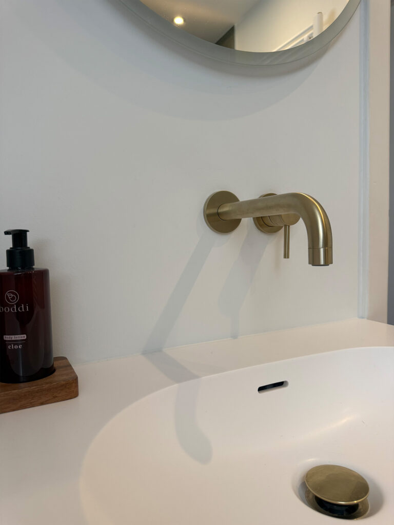 Wastafel in witte Solid Surface met geborsteld goud Nobili-kraan en ronde spiegel in Brusselse badkamerrenovatie