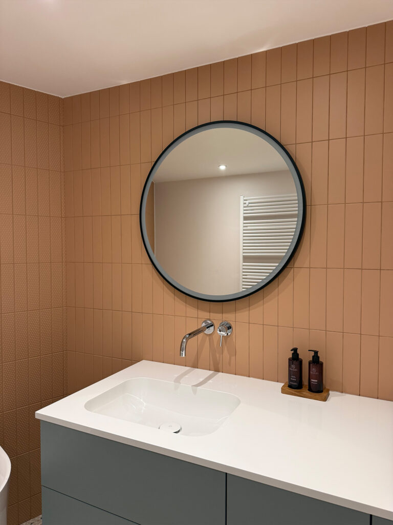 Wastafel in witte Solid Surface met geborsteld goud Nobili-kraan en ronde spiegel in Brusselse badkamerrenovatie